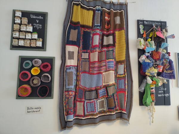 Diverse an der Wand befestigte Werke, die mit Hilfe von Upcycling im Atelier Mitzi hergestellt wurden. Darunter eine Patchwork-Decke, mehrere gehäkelte Körbe und ein "Wertstoffbaum".