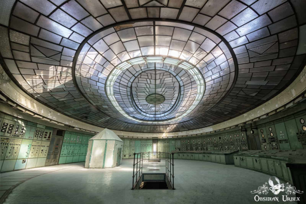 art deco control room, oval with immense skylight. Stairs lead down, there is a curved control panel on the right covered with dials and switches (the walls on both sides are similarly covered). There is a concrete bunked to the center left
