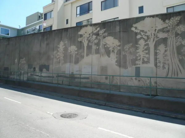 A city wall, dark with dirt yet cleaned in places to show a complex landscape with trees