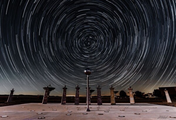 2018 July 13

Star Trails and the Bracewell Radio Sundial
 * Image Credit & Copyright: Miles Lucas at NRAO

Explanation: 
Sundials use the location of a shadow to measure the Earth's rotation and indicate the time of day. So it's fitting that this sundial, at the Very Large Array Radio Telescope Observatory in New Mexico, commemorates the history of radio astronomy and radio astronomy pioneer Ronald Bracewell. The radio sundial was constructed using pieces of a solar mapping radio telescope array that Bracewell orginaly built near the Stanford University campus. Bracewell's array was used to contribute data to plan the first Moon landing, its pillars signed by visiting scientists and radio astronomers, including two Nobel prize winners. As for most sundials the shadow cast by the central gnomon follows markers that show the solar time of day, along with solstices and equinoxes. But markers on the radio sundial are also laid out according to local sidereal time. They show the position of the invisible radio shadows of three bright radio sources in Earth's sky, supernova remnant Cassiopeia A, active galaxy Cygnus A, and active galaxy Centaurus A. Sidereal time is just star time, the Earth's rotation as measured with the stars and distant galaxies. That rotation is reflected in this composited hour-long exposure. Above the Bracewell Radio Sundial, the stars trace concentric trails around the north celestial pole. 

Authors & editors: Robert Nemiroff (MTU) & Jerry Bonnell (UMCP)
