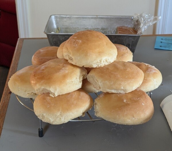 Picture of a pile of about a dozen homemade hamburger buns cooling down on a circular rack.
They look a bit flat and have no sesame on them but they're nicely golden.