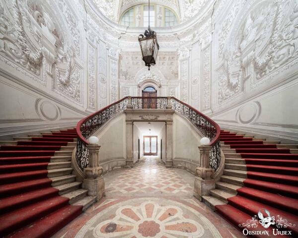 double stairs with red carpets, a lantern hanging and the walls are painted to look like columns and reliefs