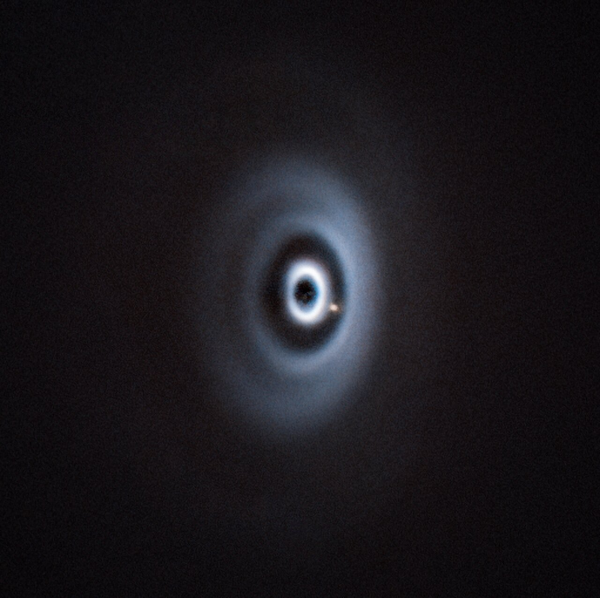 A white protoplanetary disc at the centre of the picture takes up most of the frame. The elliptical cloud of dust and gas consists of several concentric rings and gaps. In one of the larger gaps there is a little dot: a planet.