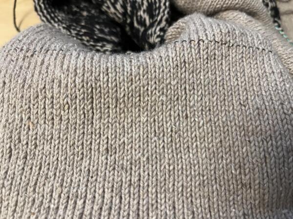 Closeup of knit garment in stockinette stitch. There are places where a column of stitches is ever so slightly further from the next.