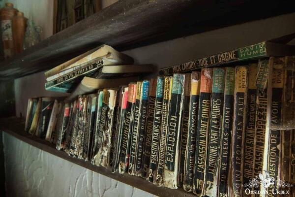 A close-up view of old, worn books with black spines and faded text lined up on a wooden shelf; some books are stacked horizontally.