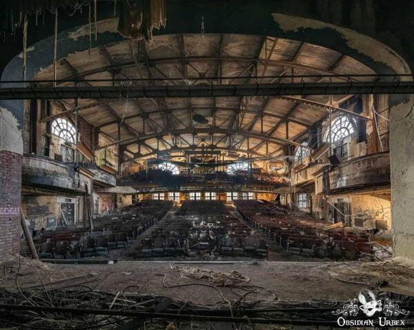 An abandoned theater shows rows of seats facing a stage covered in debris. The structure's age and disrepair is apparent throughout, with peeling paint and damaged architecture.
