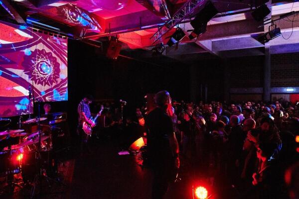 Der Winteraward. Eine Band spielt auf einer Bühne mit Schlagzeug, Gitarre und Gesang. Vor der Bühne steht ein dicht gedrängtes Publikum. Die Bühne ist mit farbigem Licht und einer großflächigen Projektion im Hintergrund ausgeleuchtet. 