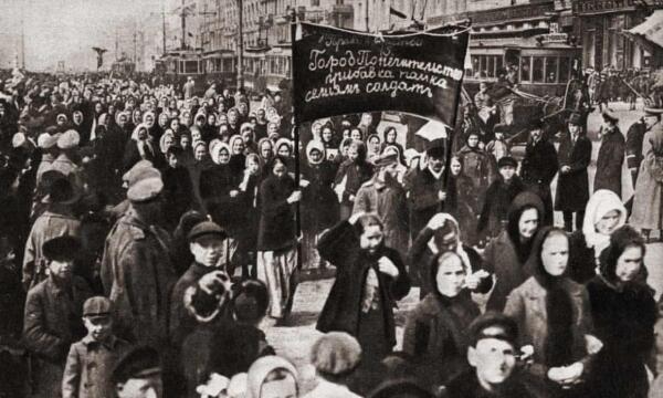 Female protesters in Petrograd on March 8, 1917, in head scarves and coats, with a banner, marching past street cars and male supporters. 