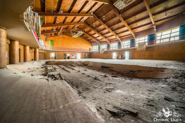 A damaged, abandoned school gym in Fukushima, Japan, after the 2011 tsunami. The wooden floor is heavily warped and broken.