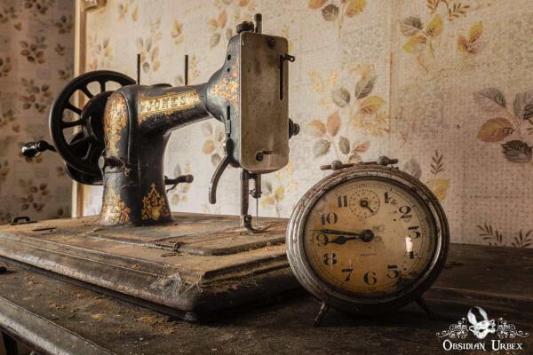A dusty vintage Jones sewing machine and an old Bayard alarm clock sit on a table against floral wallpaper.