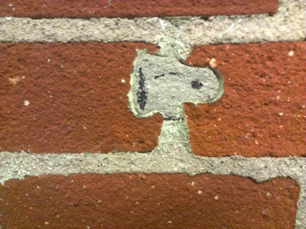 A piece of creative street art where a brick wall's mortar joint has painted to look like Snoopy, eyes closed